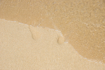 Traces of a man on a sandy beach and a sea wave erasing them.