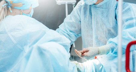 Surgeon performing surgery on breasts in hospital operating room. Surgeon in mask wearing surgical...