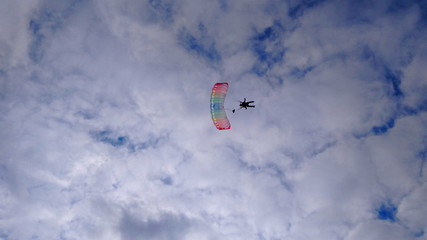 Silhouette of a skydiver in the sky against a blue sky with white clouds with a multicolored parachute