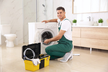 Professional plumber repairing washing machine in bathroom