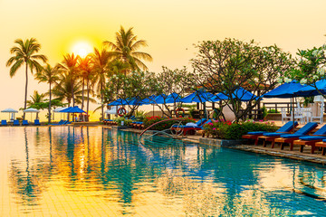 Fototapeta na wymiar palm tree with umbrella chair pool in luxury hotel resort at sunrise times