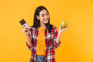 Image of cheerful woman smiling while holding apple and chocolate