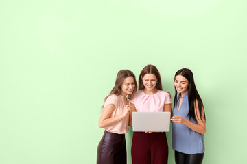 Beautiful young businesswomen with laptop on color background