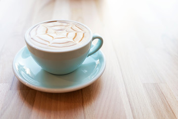 Morning coffee in a blue cup on a wooden background with copy space. Cappuccino with light from a window. Relax and break. Aroma beverage. 