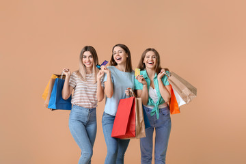 Young women with credit cards and shopping bags on color background