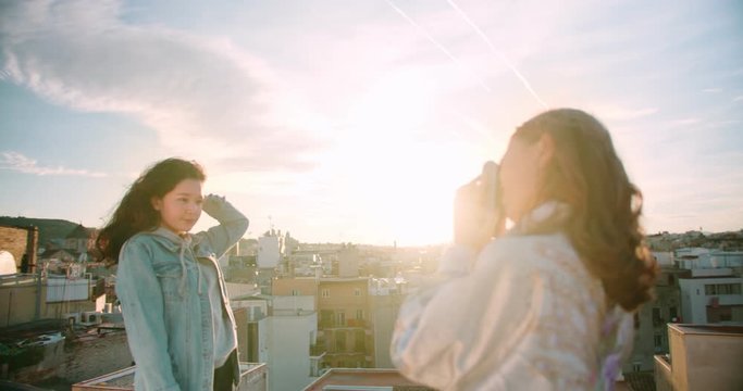 Charming natural Asian girl posing for friend photo standing on rooftop outdoor sunny, young teen female using camera taking picture spending happy time together outside with urban view Barcelona