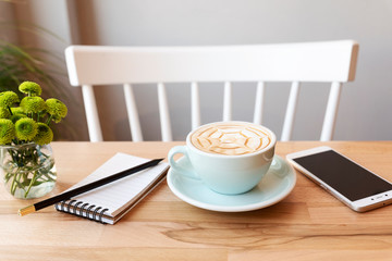 Coffee cup with notebook, pencil and mobile phone on a wooden table in cafe with wooden chair. Relax and chill out in coffee shop. Nobody.