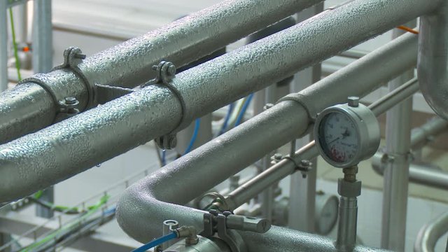 Steel, modern, shiny pipeline is covered with droplets of condensate. Pressure gauge, measuring instrument. Modern equipment on ice cream factory. Modern equipment on ice cream factory.