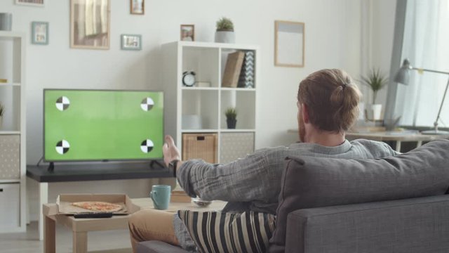 Back view of emotional Caucasian man wearing casual clothes sitting in living room at TV and watching football match