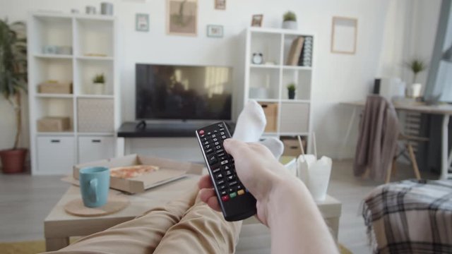 Back view of hand of unrecognizable person holding remote controller and switching TV channels