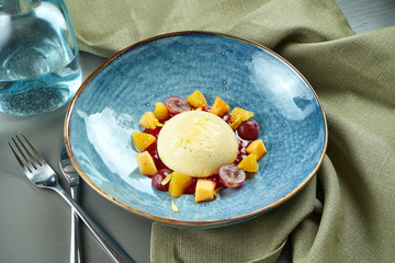 Panna Cotta - a delicious and beautiful dessert made of cream and vanilla with grapes and peach in a blue bowl on a wooden background. Italian cuisine
