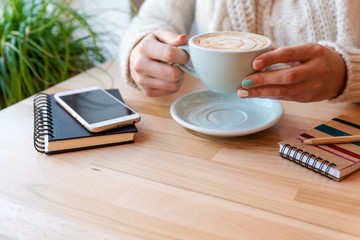 Woman with cup of coffee and phone on a wooden table with copy space. Morning coffee in cafe with space on a background. Close up
