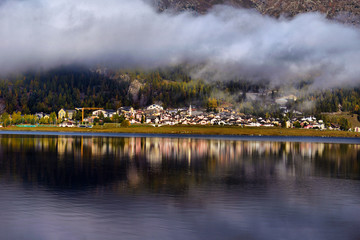 Fototapeta premium Mountain lake at sunrise in autumn. Landscape with lake, gold sunlight, blue fog over the water, reflection, trees with colorful leaves