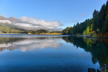 Mountain lake at sunrise in autumn. Landscape with lake, gold sunlight, blue fog over the water, reflection, trees with colorful leaves