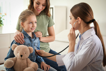 Mother and daughter visiting pediatrician. Doctor examining little patient with stethoscope in...