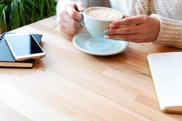 Woman hands with coffee in the morning in cafe and wooden table with copy space. Phone and notebook during business meeting with space for your text. 