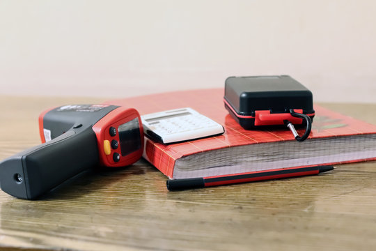 A journal for notes, a calculator, a fountain pen and a laser temperature sensor are on the table.