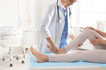 Female orthopedist examining patient's leg in clinic, closeup - obrazy, fototapety, plakaty