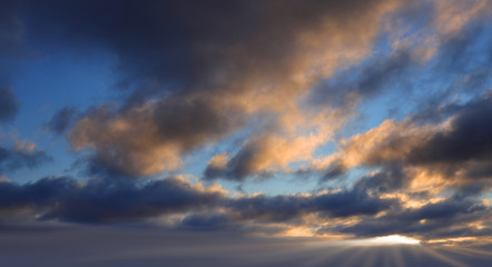 Dark clouds illuminated by the evening sun with gleams of blue sky and sunbeams.