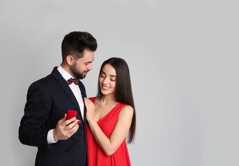 Man with engagement ring making marriage proposal to girlfriend on light grey background
