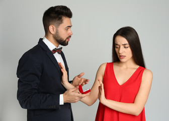 Young woman rejecting engagement ring from boyfriend on light grey background