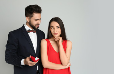 Man with engagement ring making marriage proposal to girlfriend on light grey background