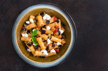 Italian pasta - Pasta alla Norma, made with macaroni, tomatoes, fried eggplants, ricotta cheese and basil. Top view. Dark concrete background