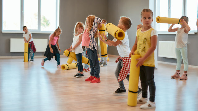 Waiting for the teacher. Group of cute children in casual clothes holding yoga mats and waiting for yoga class in the dance studio