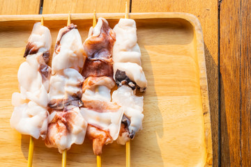 Fresh cut squid on skewers in a wooden tray on a wooden table