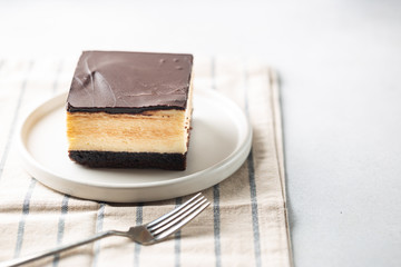 Piece of cake with souffle Birds milk, biscuit, mousse and dark chocolate on a white plate, light background