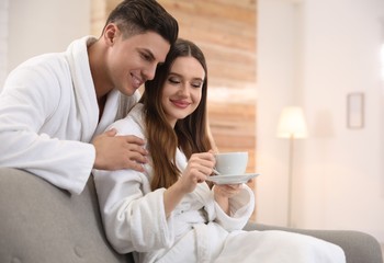 Obraz na płótnie Canvas Man in bathrobe hugging his girlfriend with coffee at home