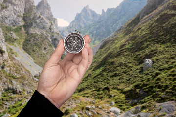 hand holding a compass with a background behind a mountainous landscape