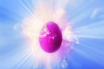 Violet egg in ink water splash and rays of light over blue background