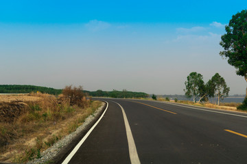 Fototapeta premium The asphalt road that is straight ahead is curved. Along the side of the road were trees, grass, and rivers. Path around the reservoir at Dok Krai Rayong Thailand.