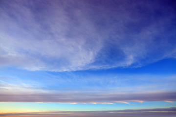 Obraz premium Blue sky background with light white clouds at the zenith and long stripes of clouds on the horizon.