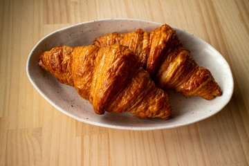Two delicious croissant on a white plate on a wooden table 1　木のテーブルの上の白い皿にのった美味しそうな二つのクロワッサン