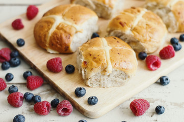 Traditional hot cross buns served with bluberry and raspberry on wooden cutting board. Easter pastry