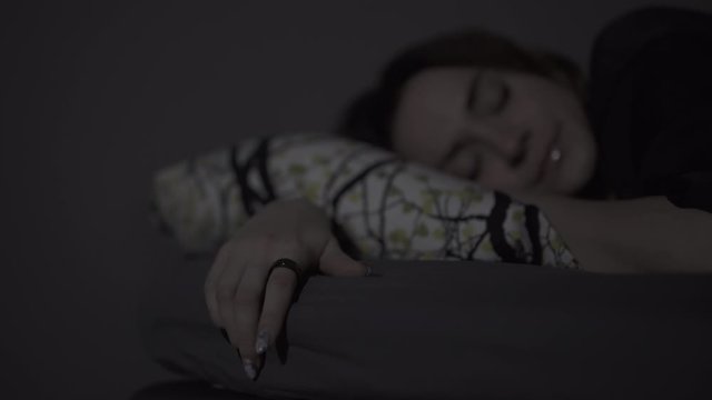 White woman with brunette hair sleeping with a smart ring on her finger, tracking her sleep.