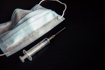 Medical face mask, disposable syringe isolated on black background, close-up. Medical supplies with...