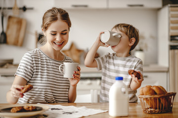 preparation of family breakfast. mother and child son cut bread  and eat cookies with milk in morning - obrazy, fototapety, plakaty