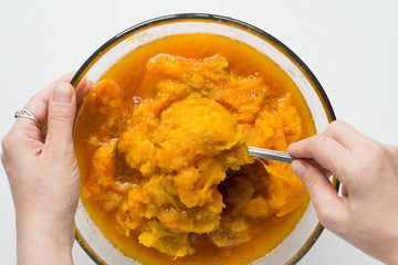 Woman hands mixing pumpkin puree in glass bowl on the white background