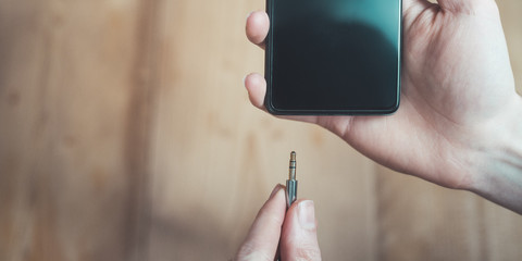 Audio jack concept: Connecting audio jack to a black mobile phone, close up
