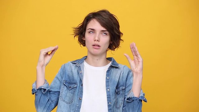 Boring fun cute brunette young woman in denim jacket white t-shirt posing showing blah blah gesture ja jaja hands isolated on yellow background in studio. People sincere emotions, lifestyle concept