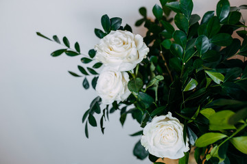 Floral composition in interior. Bunch with white roses and green leaves.