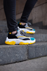 Feet shod in multi-colored sneakers of yellow, white, black and blue on the marble stairs