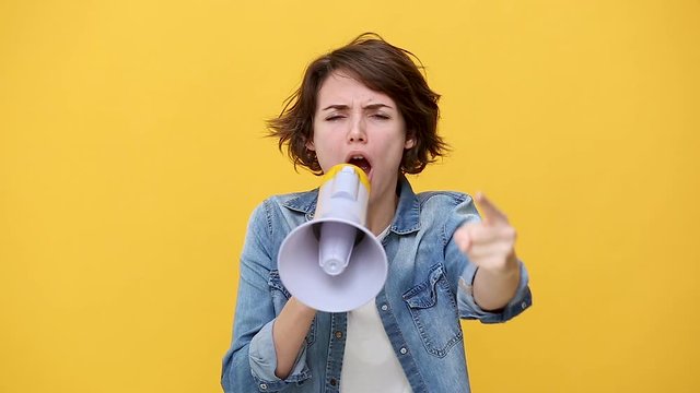 Angry sad young woman in denim jacket white t-shirt posing isolated on yellow background in studio. People sincere emotions lifestyle concept. Scream in megaphone, protest for better future, Hurry up