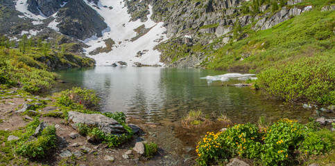 Spring in the mountains. Snow on the slopes, green meadows, lake.