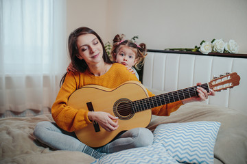 Mother and daughter playing in the bed. Mother playing guitar for daughter on the bed.