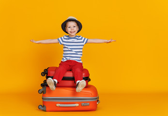 cheerful boy traveler with suitcase on colored yellow background.