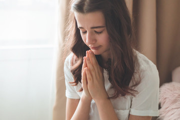 Teenager Girl closed her eyes, praying in a in the living room. Hands folded in prayer concept for faith, spirituality and religion. Peace, hope, dreams concept